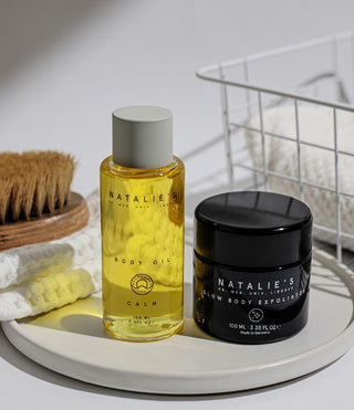 Calm body oil and glow body exfoliator standing next to each other on a ceramic plate